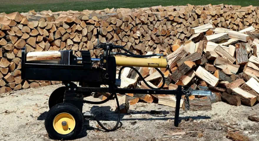 Czarna piło łuparka z żółtym cylindrem hydraulicznym stoi obok stosów drewna opałowego.