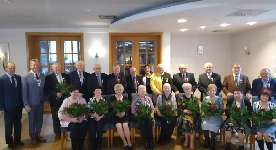 Grupa osób świętuje 50 rocznicę ślubu. Wszyscy otrzymują róże i medale.