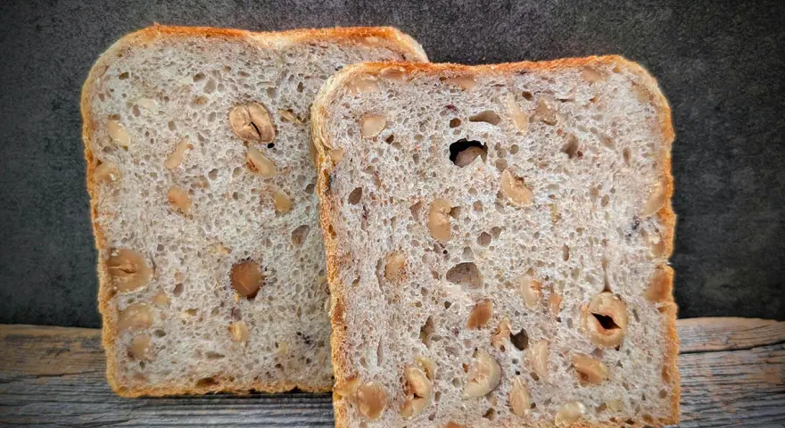 Zwei Scheiben salzarmes Brot mit Nüssen liegen auf Holz.