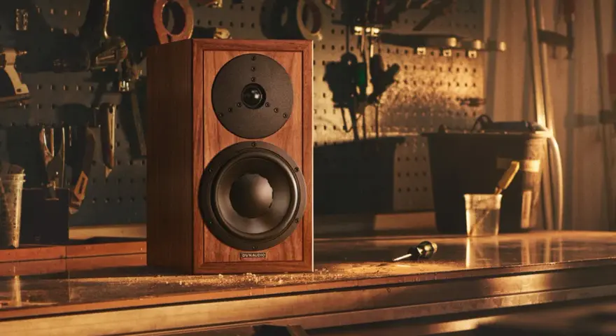 Głośnik Dynaudio Special 25 w drewnianej obudowie, stojący na stole w warsztacie, otoczony narzędziami.