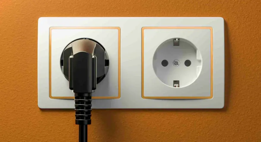 Dwa gniazdka elektryczne, jedno z wtyczką, na pomarańczowej ścianie. Typowe gniazdka w Hiszpanii.