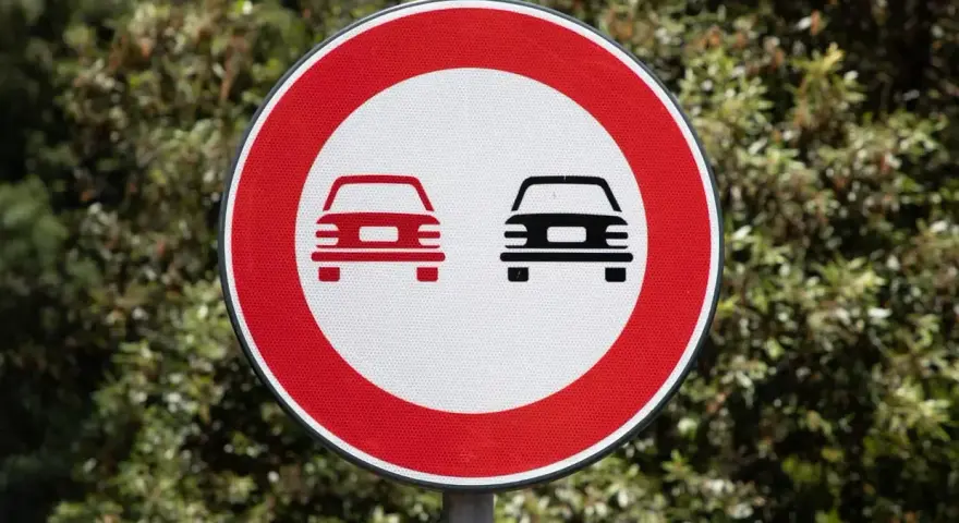 Segnale stradale art. 148: divieto di sorpasso per autoveicoli. Due auto stilizzate, una rossa e una nera, su sfondo bianco e bordo rosso.