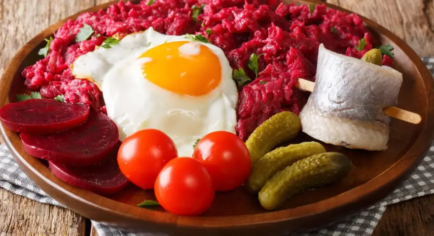 Labskaus: was ist das? Ein deftiges Gericht mit Roter Bete, Kartoffeln, Corned Beef, Spiegelei, Rollmops und Gewürzgurken.