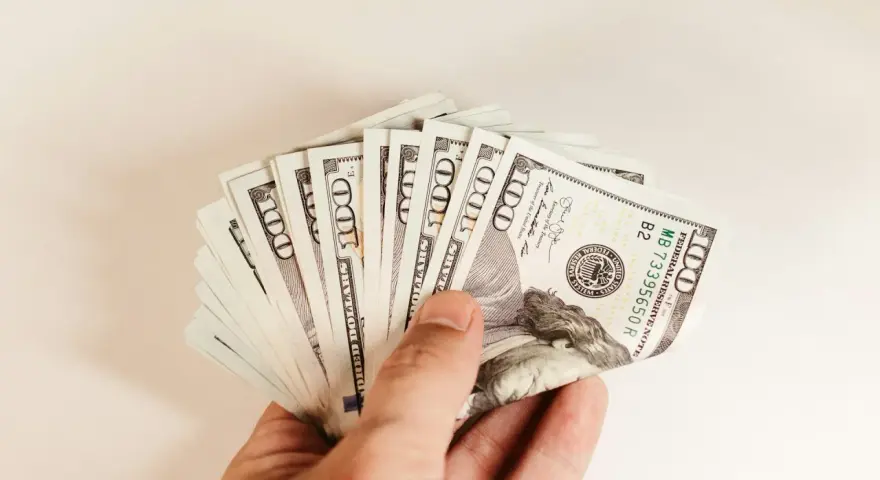 Dłoń trzyma plik banknotów 100 dolarowych. To może być kwota na spłatę PCC od pożyczki.