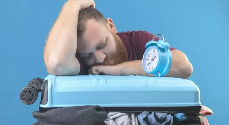 Zmęczony podróżnik śpi na walizce obok budzika. Czy to jetlag?