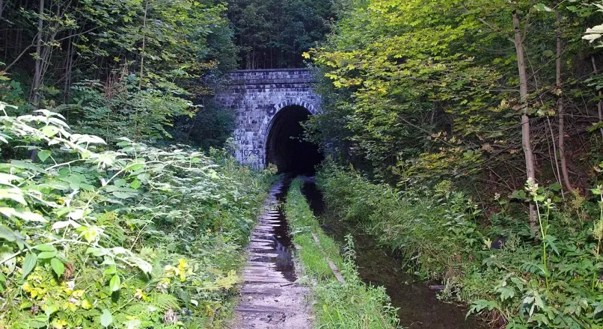 Kamienna, kameralna brama do mrocznego tunelu kolejowego w Kowarach, otoczona bujną zielenią.