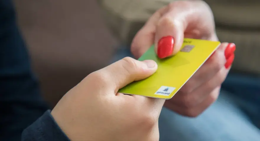 Eine Hand gibt einer anderen eine gelbe Girocard. Dies könnte die erste kinder debitkarte sein, die ein Kind erhält.