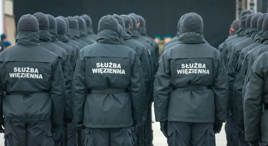 Grupa funkcjonariuszy Służby Więziennej w mundurach, widok od tyłu.