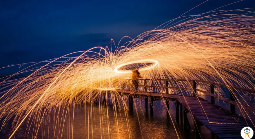 Une personne sur un pont crée une **light painting photo** spectaculaire avec des traînées de feu dans le ciel nocturne.