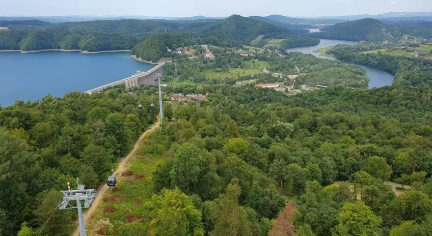 Widok na zielone wzgórza nad Soliną, z widoczną zaporą, jeziorem i kolejką gondolową. Trasa widokowa zachwyca.