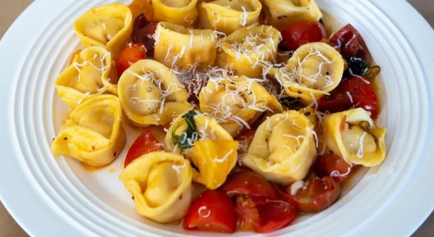 Pyszne tortellini z pomidorkami i parmezanem na białym talerzu. Idealne danie, czy ravioli czy tortellini?
