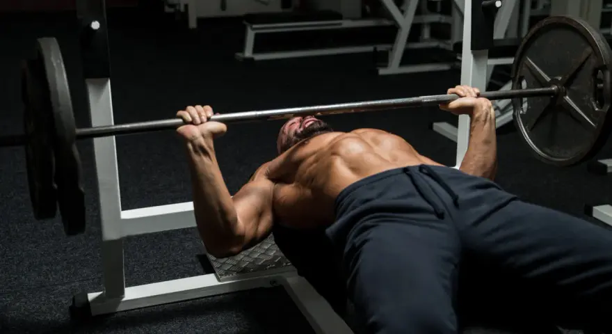 Man med skägg och synliga muskler utför bänkpress som en del av sitt starting strength program.