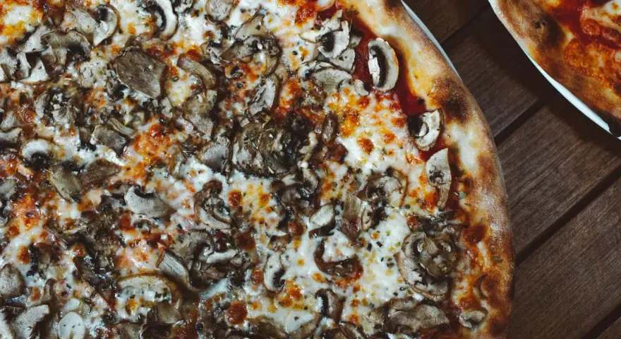 Pyszna pizza wegetariańska z pieczarkami i ciągnącym się serem, idealna na wspólny wieczór.