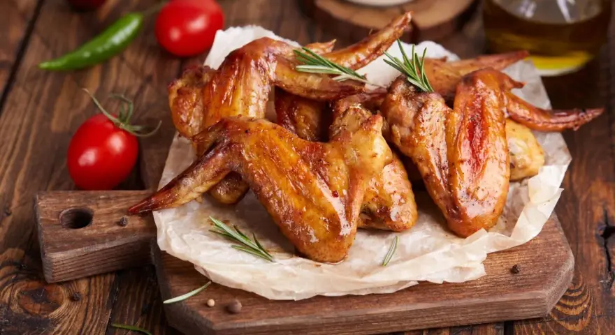 Alette di pollo dorate e succulente, cotte alla perfezione nella friggitrice ad aria, servite su carta forno con rosmarino, pomodorini e peperoncino.