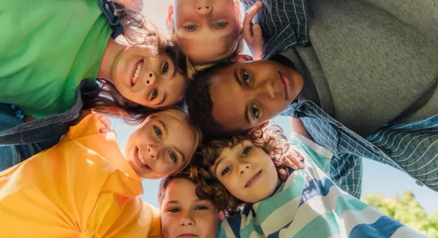 Un groupe d'enfants souriants forme un cercle, leurs visages se rejoignant au centre. Leurs regards joyeux et leurs expressions témoignent d'un bel encadrement d'enfants.