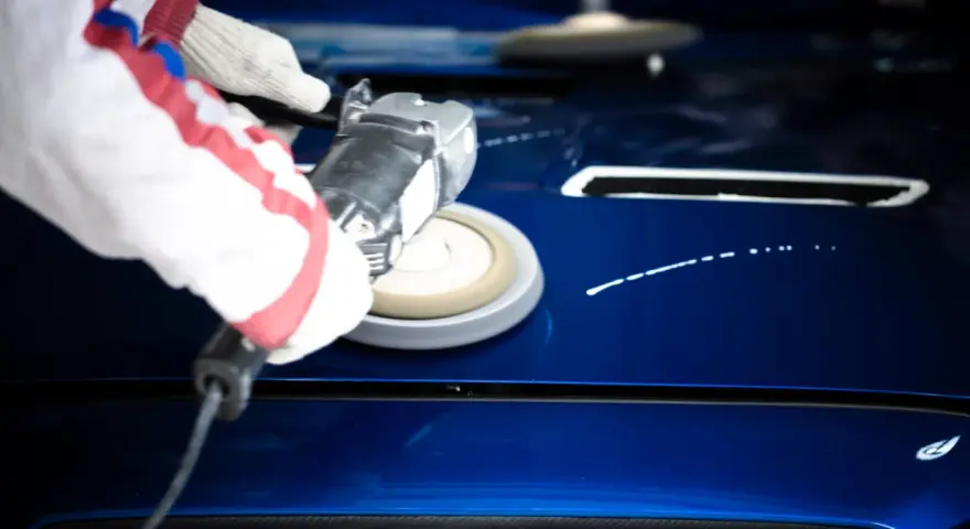 A gloved hand uses a buffer to polish a shiny blue car hood, demonstrating how to polish a car with a buffer for a flawless finish.