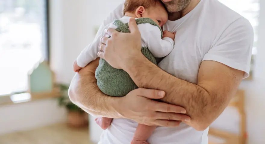 Ojciec czule tuli noworodka, podnosząc go pod pachy. Od kiedy tylko się urodził, czuje tę niezwykłą więź.