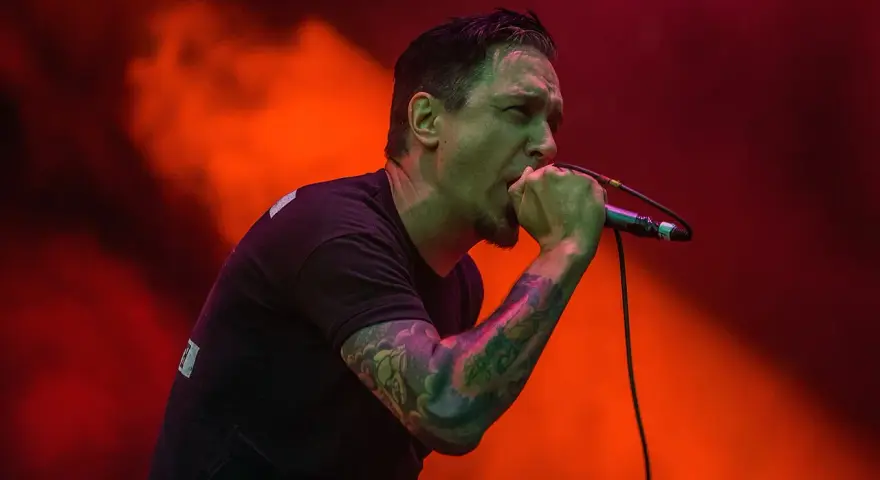 Chanteur au micro, le regard intense, comme s'il en avait marre de tout. Lumières rouges et orangées.