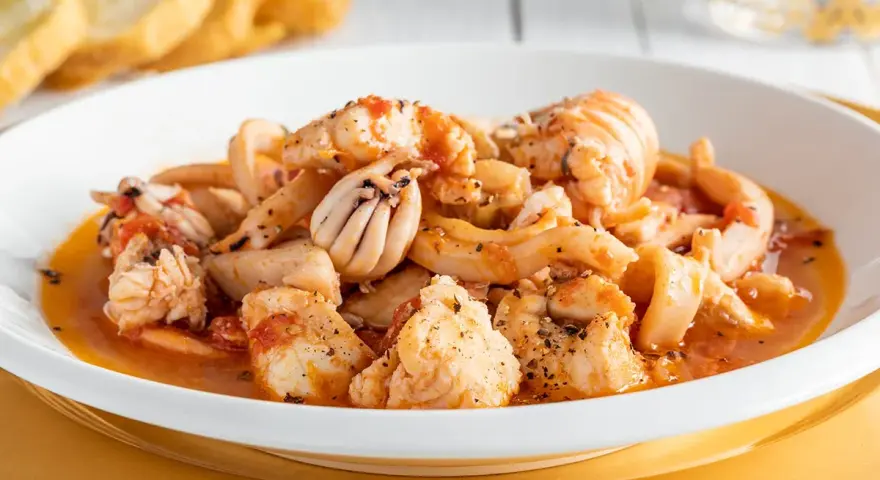 Un invitante piatto di zuppa di pesce, ricco di calamari, gamberi e pesce bianco, servito con crostini dorati.