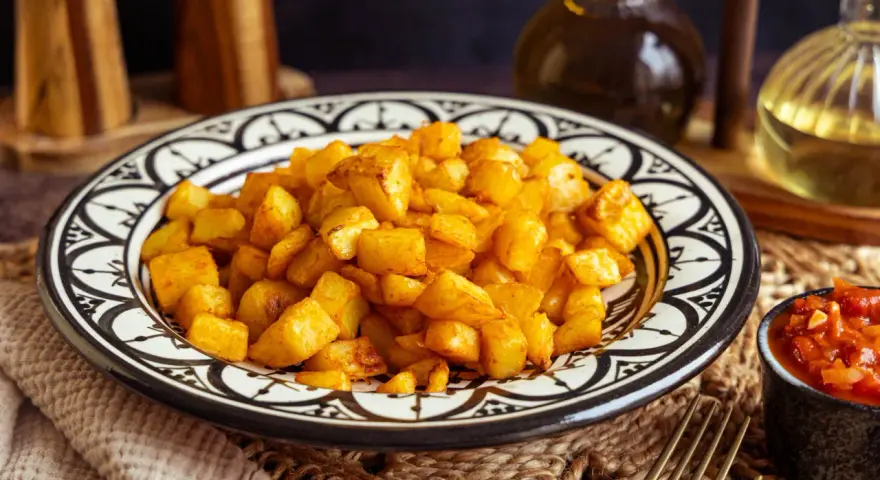 Knusprige patatas bravas in einer marokkanisch inspirierten Schale, daneben eine Schale mit scharfer Tomatensauce.