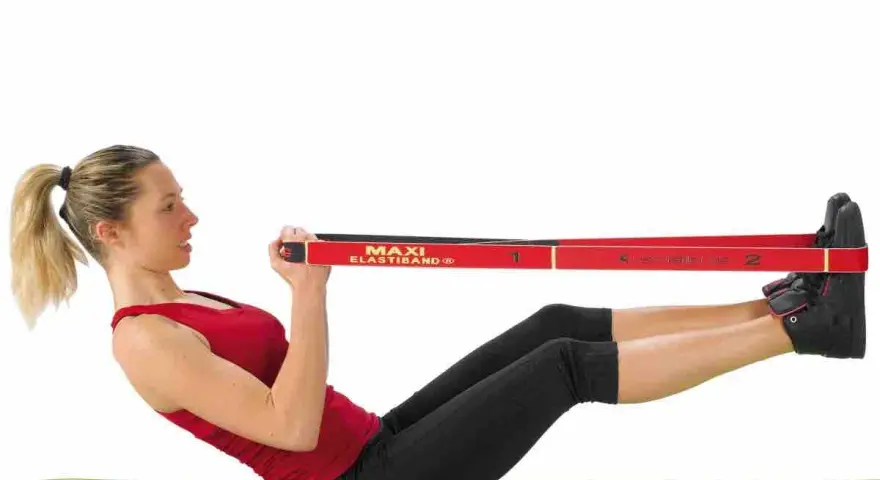 Femme faisant un exercice avec un élastique, jambes tendues et mains tenant la bande rouge.