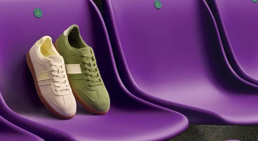 Due sneakers Clarks, una beige e una verde, sedute su sedili viola. Le Clarks calzano mezza misura in meno, perfette per un look casual.