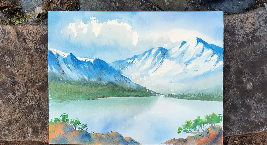 Pintura de montañas nevadas y un lago sereno, mostrando como se pinta con acuarela. Nubes blancas flotan en un cielo azul.