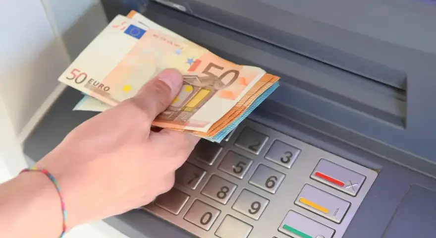 Dłoń trzyma banknoty 50 euro przy bankomacie. W Hiszpanii, jak w całej strefie euro, obowiązuje euro.