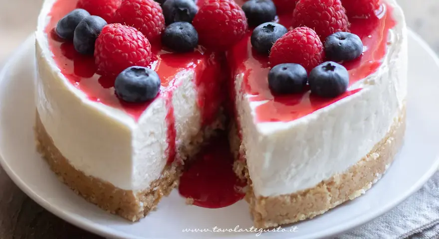 Delizioso cheesecake con mascarpone, guarnito con lamponi freschi, mirtilli e una cascata di salsa rossa.