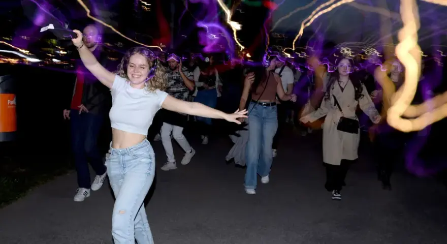 Junge Leute mit Kopfhörern, die im Dunkeln tanzen gehen, umgeben von bunten Lichtspuren.