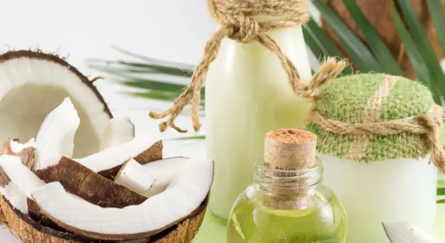 Aceite de coco para el pelo en frascos y botellas, junto a cocos frescos y hojas verdes.