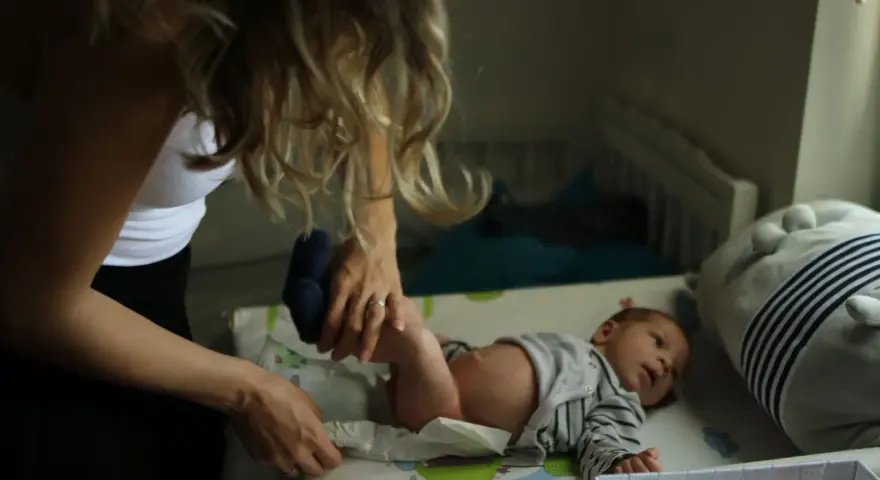 Mama zmienia pieluszkę noworodkowi. Zastanawiasz się, ile kupić pieluszek dla noworodka? Warto mieć zapas!