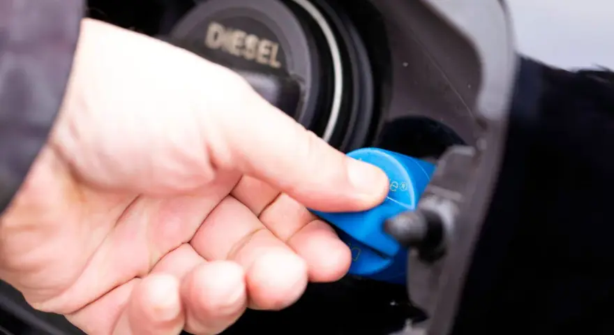 Hand schraubt blauen AdBlue-Deckel auf Diesel-Tanköffnung. AdBlue ist eine Harnstofflösung zur Abgasreinigung bei Dieselfahrzeugen.