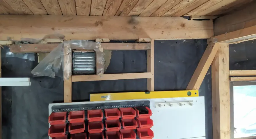 Pågår arbete för att isolera garage. Syns träbjälkar, isolering och förvaringssystem med fack.