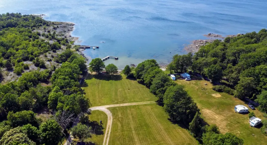 Vacker vy över camping i Blekinge med husvagnar vid en brygga och grönskande skog.
