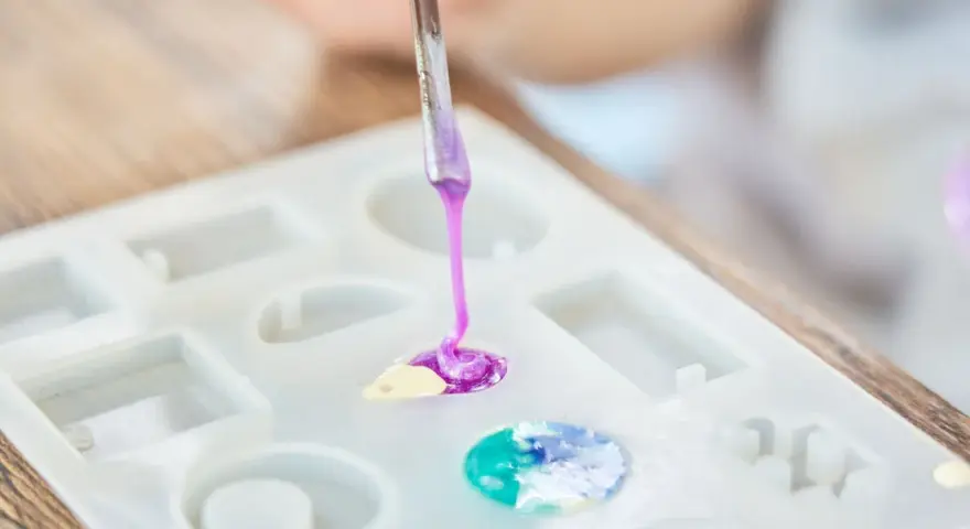 A person is learning how to make an epoxy resin mold by carefully pouring colored resin into a silicone mold.