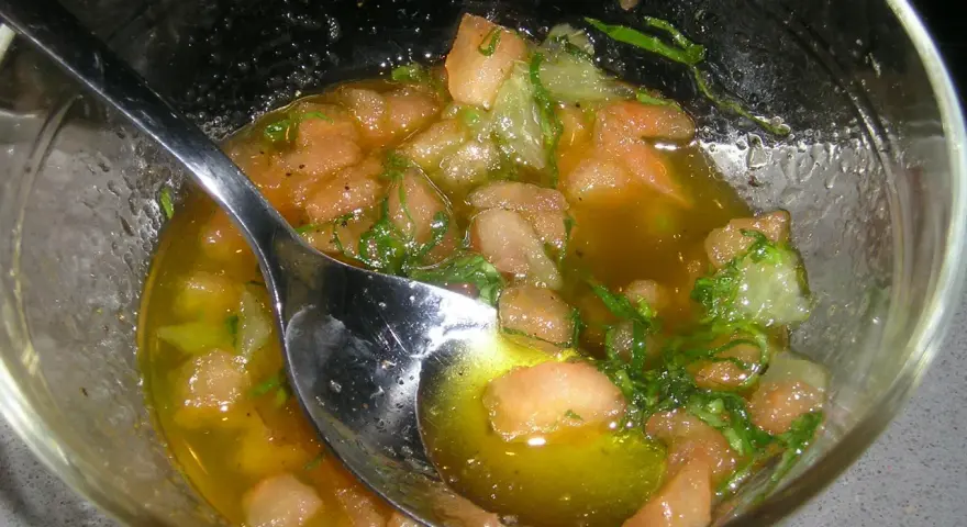 Un bol de sauce vierge recette, avec des morceaux de tomates, des herbes fraîches et une cuillère en argent.