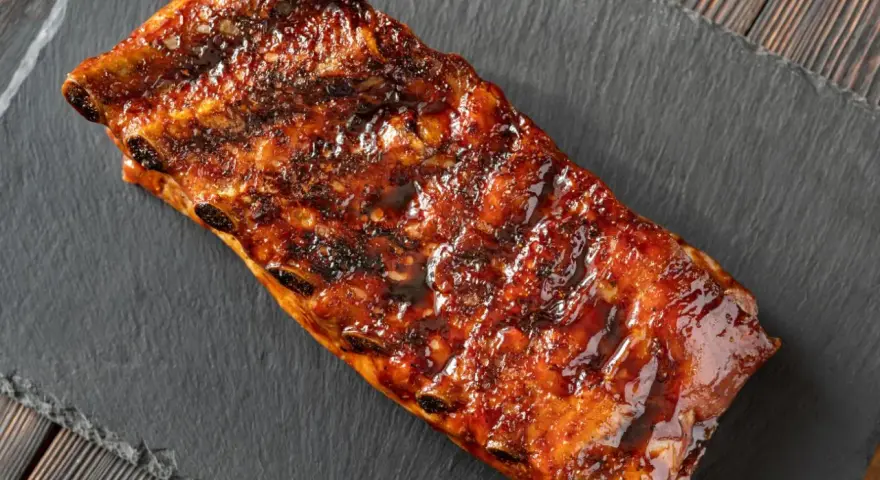 Costillas a la miel, glaseadas y jugosas, servidas sobre una pizarra oscura.
