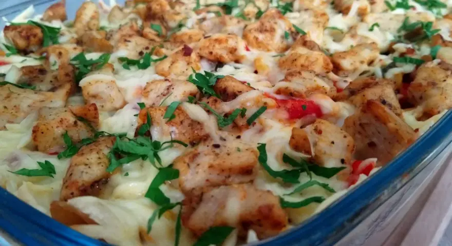 Pyszna zapiekanka gyros z makaronem, posypana serem i natką pietruszki, w szklanym naczyniu.