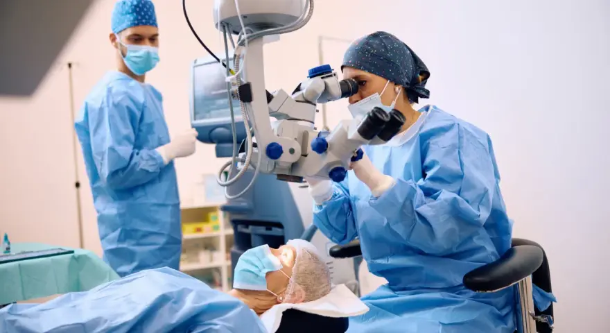 Chirurghi in sala operatoria, uno esegue una vitrectomia non riuscita con un microscopio, mentre un altro assiste.