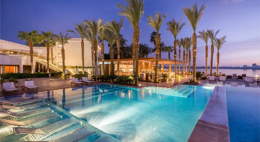 Luxury resort pool with palm trees and lounge chairs at dusk.