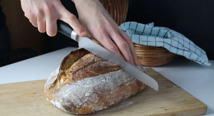 Krojenie świeżego chleba na desce. Idealna temperatura, w jakiej piec chleb, to klucz do jego chrupkości.