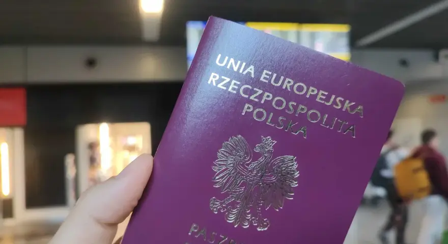 Dłoń trzyma fioletowy paszport Rzeczypospolitej Polskiej z godłem orła.