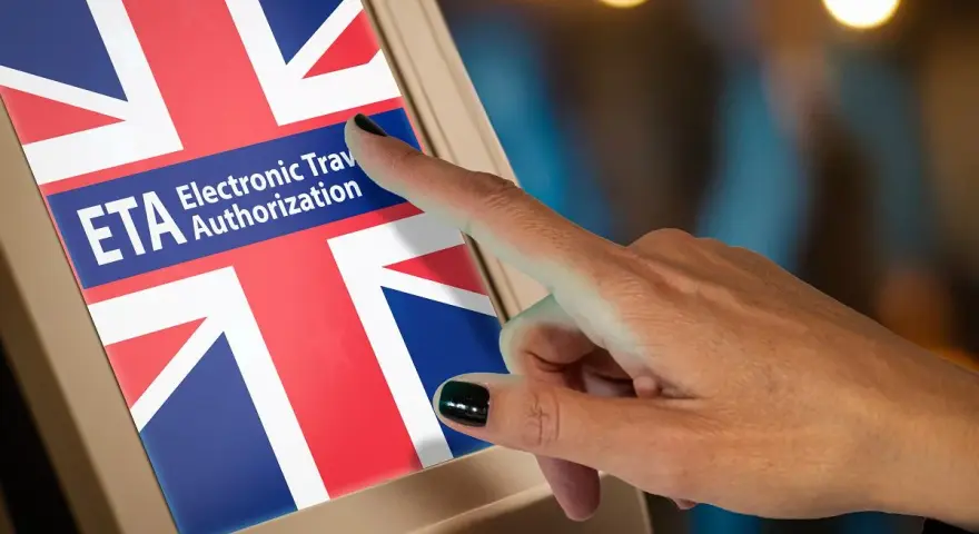Dłoń naciska ekran z flagą Wielkiej Brytanii i napisem ETA Electronic Travel Authorization. To krok do uzyskania wizy do Anglii.