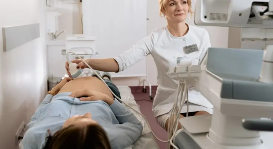 Lekarka wykonuje badania prenatalne, pokazując przyszłej mamie, jak się przygotować do wizyty.