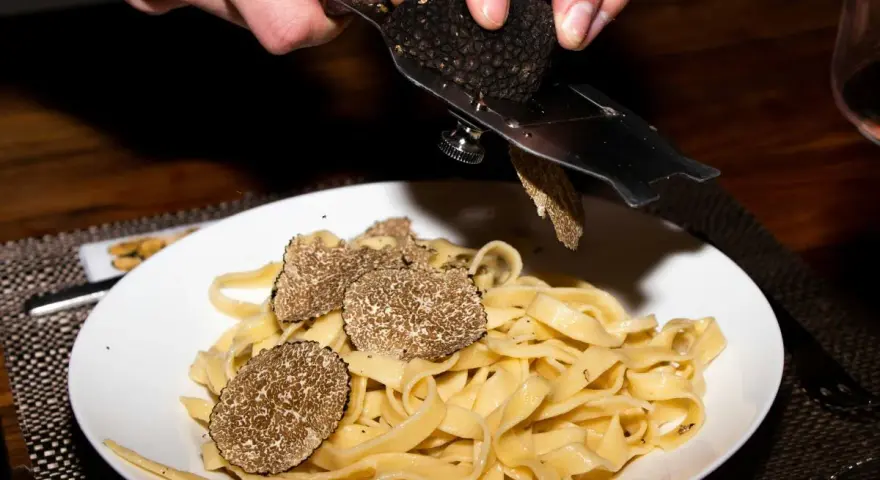 Dłonie trą całe grzyby trufle nad talerzem tagliatelle.