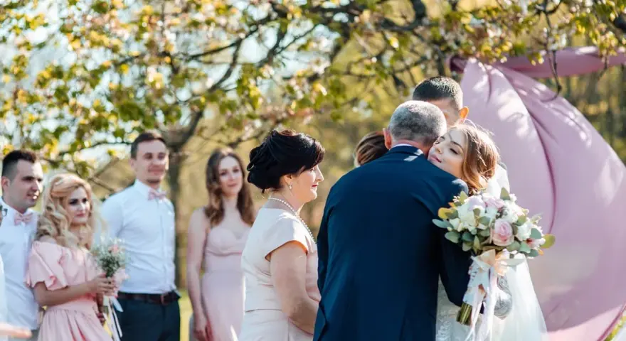 Wzruszające życzenia dla młodej pary. Panna młoda tuli się do ojca, a goście patrzą z uśmiechem.