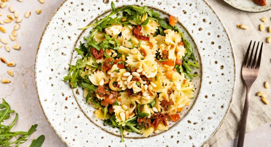 Mediterraner Salat mit Farfalle, getrockneten Tomaten, Rucola, Pinienkernen und Mozzarella.