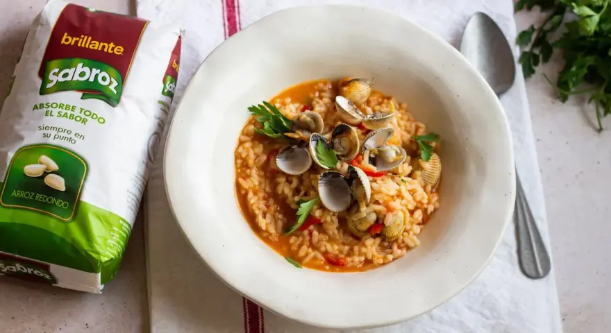 Delicioso arroz con berberechos, preparado con arroz redondo Sabroz, adornado con perejil fresco.