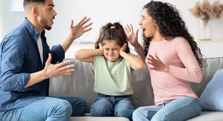 Ein Kind hält sich die Ohren zu, während die Eltern streiten. Eine Szene, die zeigt, wie schwierig es ist, wenn Eltern sich trennen.